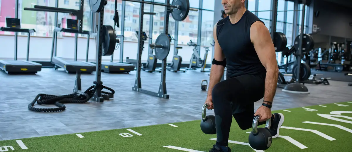 Athlete lunging with kettlebells on clean artificial training turf in a premium fitness facility