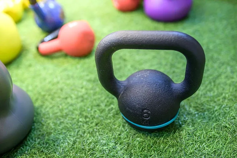 Kettlebells and dumbbells resting on clean artificial gym turf