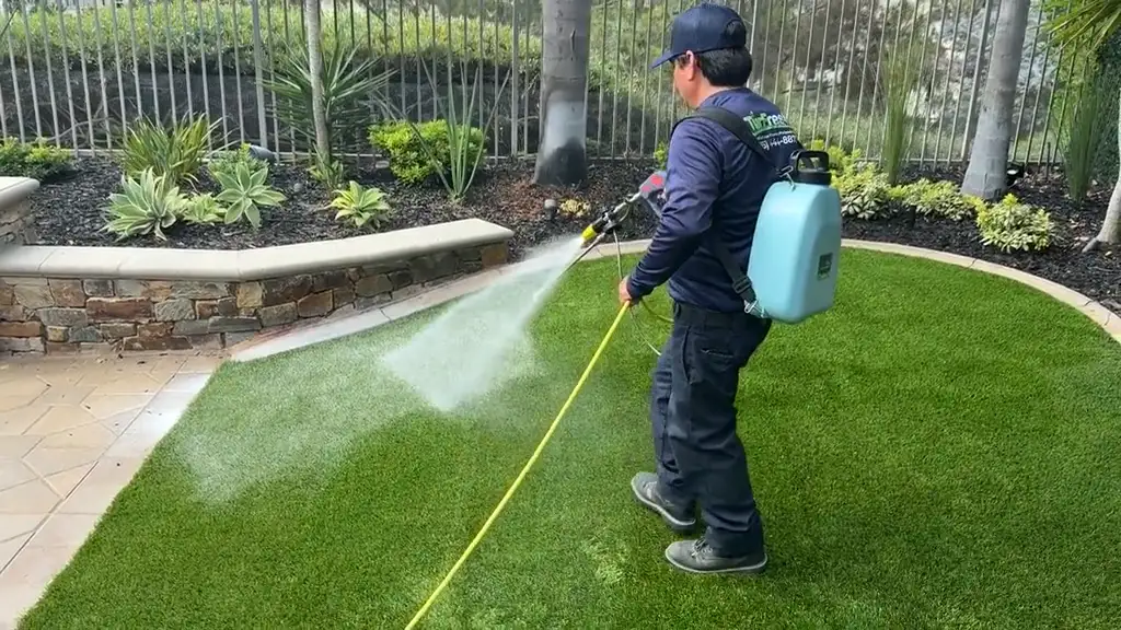 TurFresh technician applying BioX+ treatment across a clean artificial turf lawn