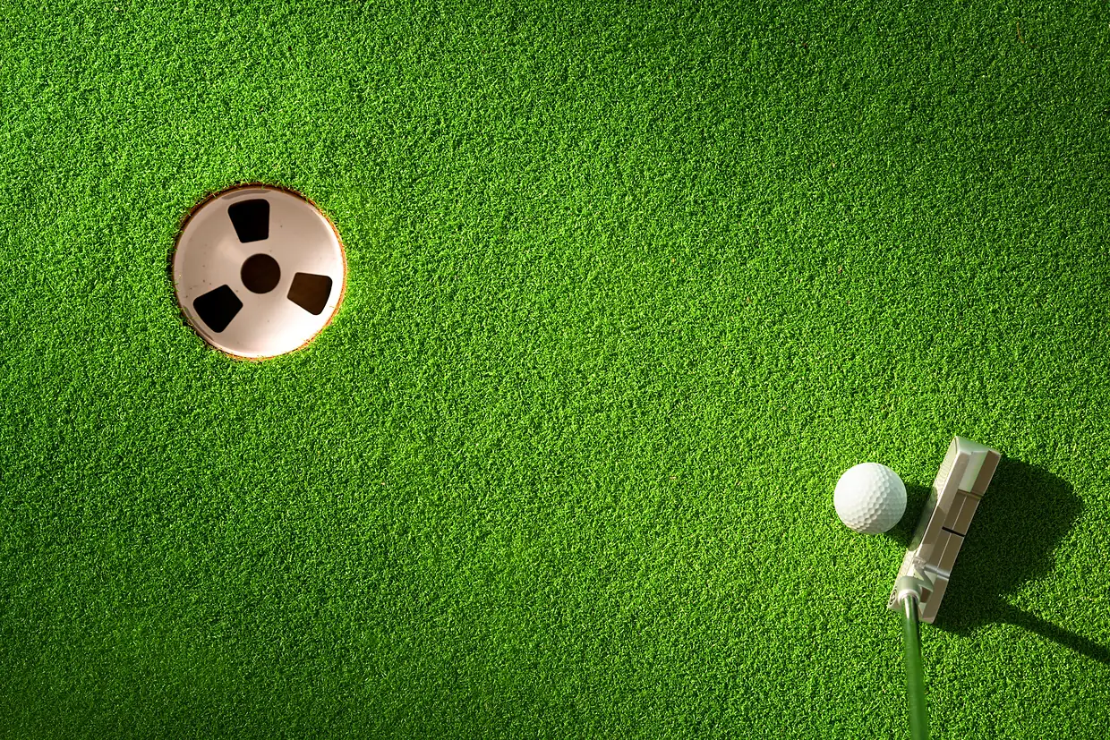 Overhead view of a clean putting green cup with ball and putter on tightly groomed turf