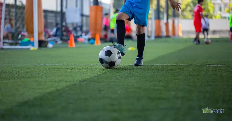 Young soccer player training on clean sanitized artificial turf field maintained with TurfAid