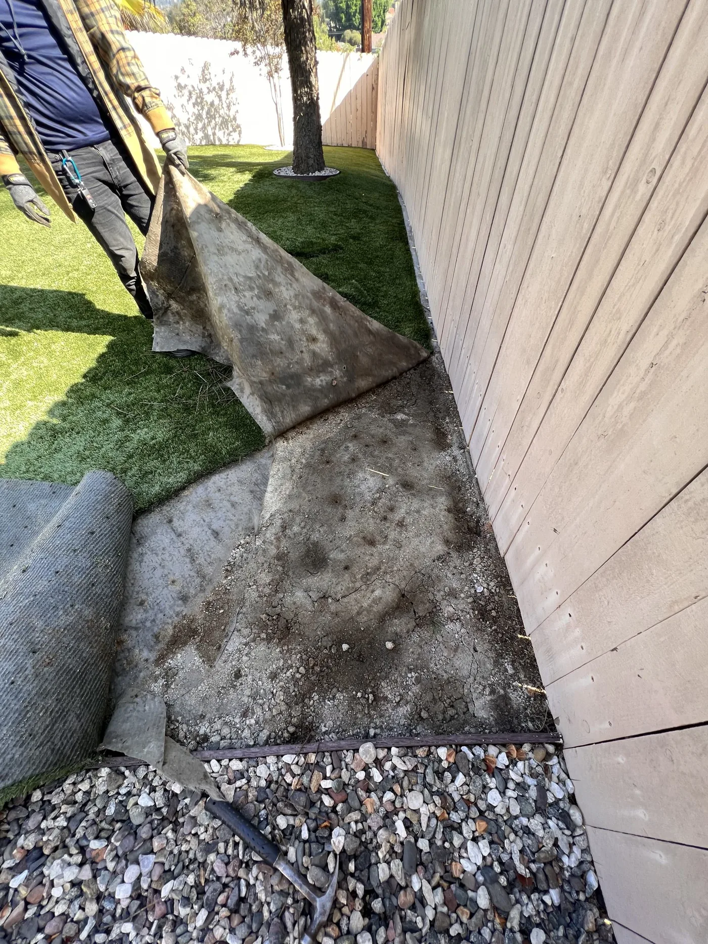 TurFix technician lifting a failed artificial turf edge along a fence line to repair the perimeter