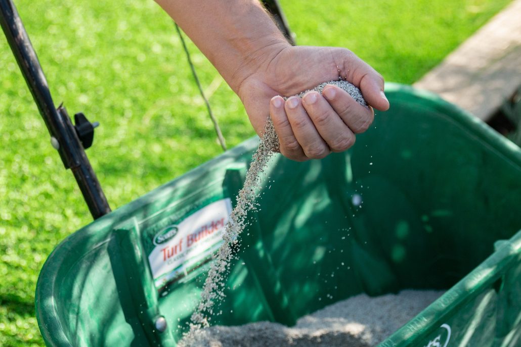 Hand pouring TurFresh TurFill infill granules into spreader for artificial grass maintenance.