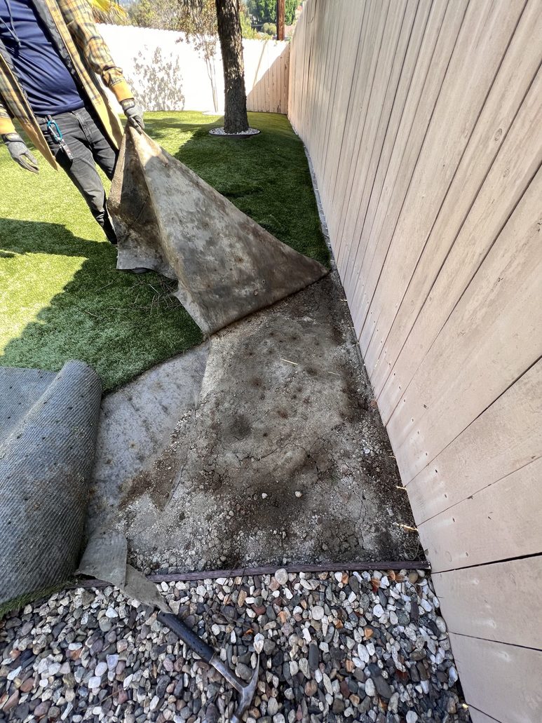 Technician lifting worn artificial turf to reveal dirt and debris buildup underneath, demonstrating the importance of TurFresh deep-cleaning service.