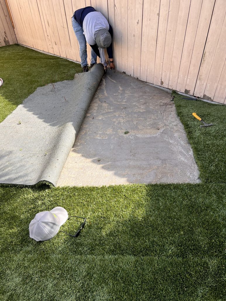 Technician lifting artificial turf for deep cleaning and restoration using TurFresh eco-friendly pet-safe solution.
