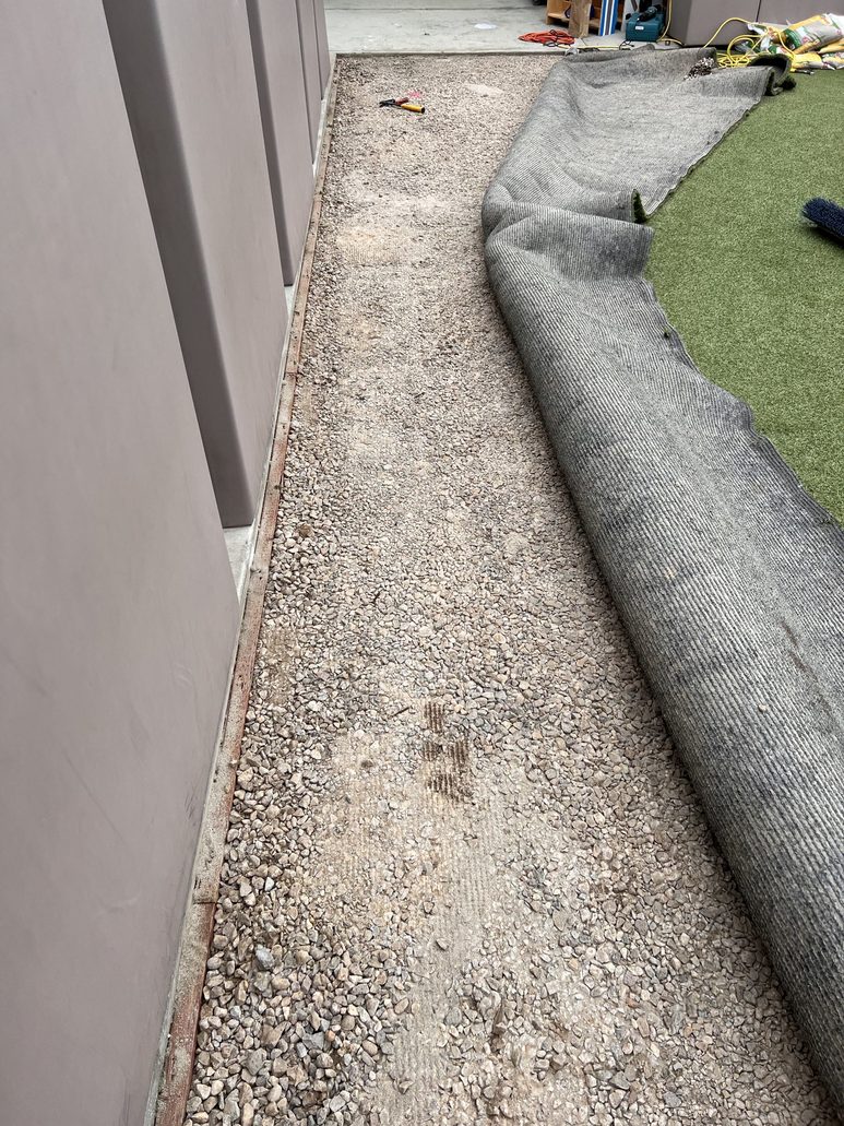 Partially lifted artificial turf exposing gravel sub-base during maintenance, highlighting TurFresh's deep-cleaning and odor-eliminating services.