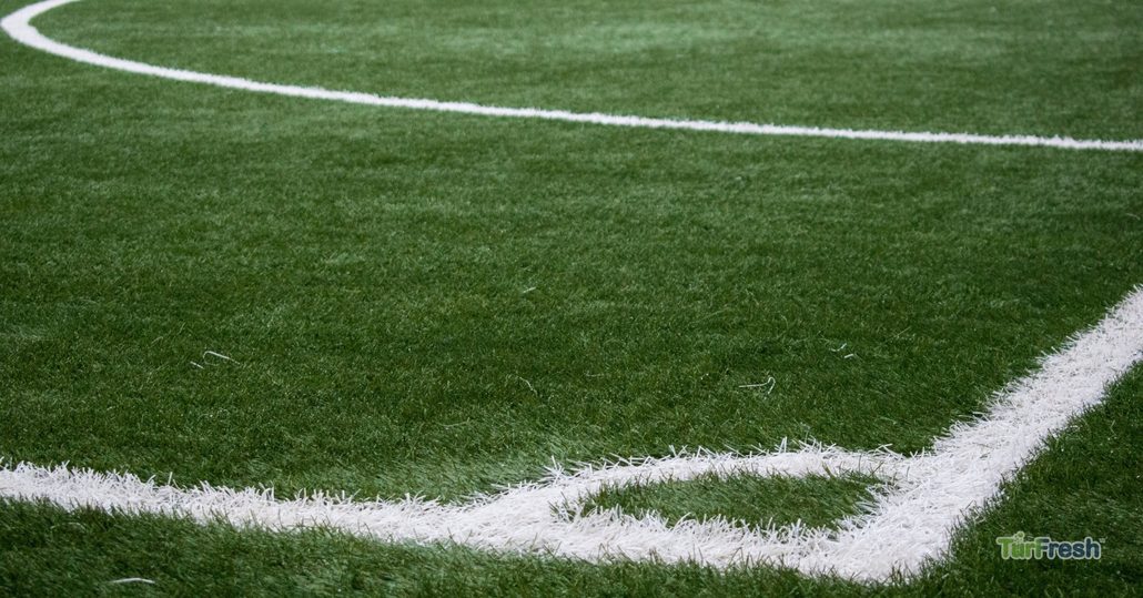 Closeup of artificial turf sports field corner with bright white lines on clean turf maintained with TurFresh professional cleaning products.
