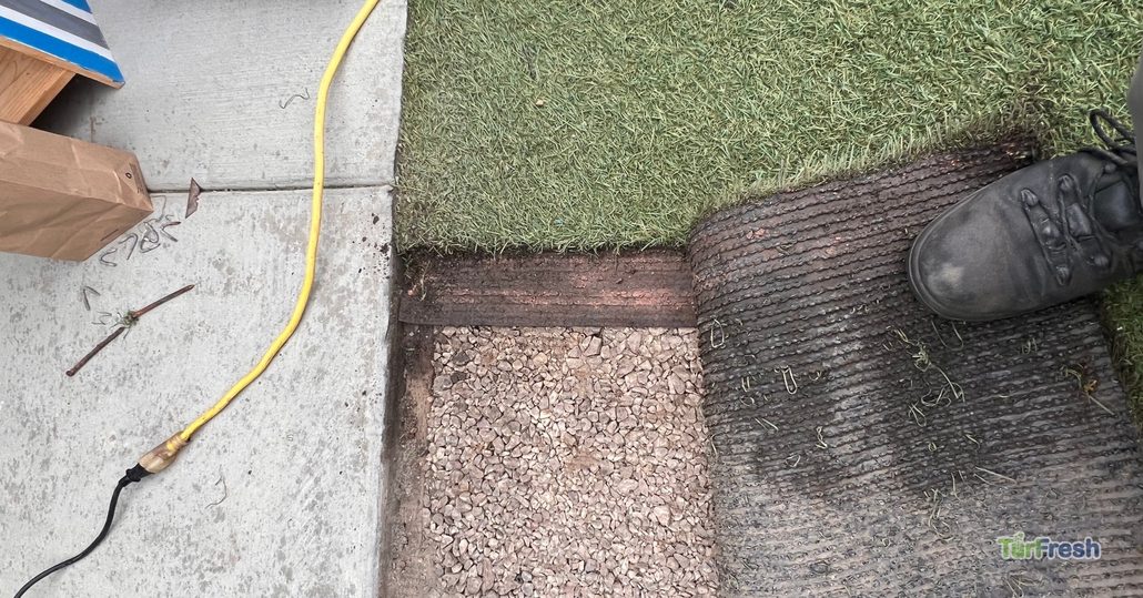 Close-up of artificial turf being lifted for maintenance, showing base layers and staples, TurFresh turf repair in progress.
