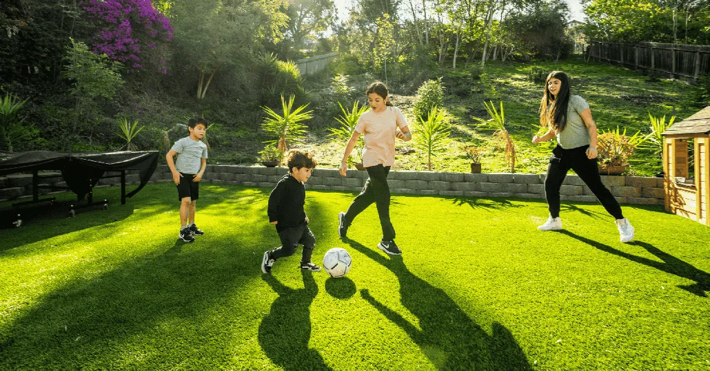 Family playing soccer on clean artificial turf maintained with TurFresh care.